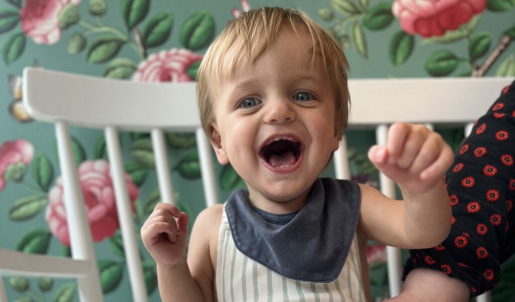 A smiling toddler in a striped romper against a green and pink floral background