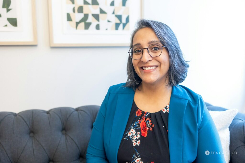 A smiling South Asian woman with glasses against an office background with the words